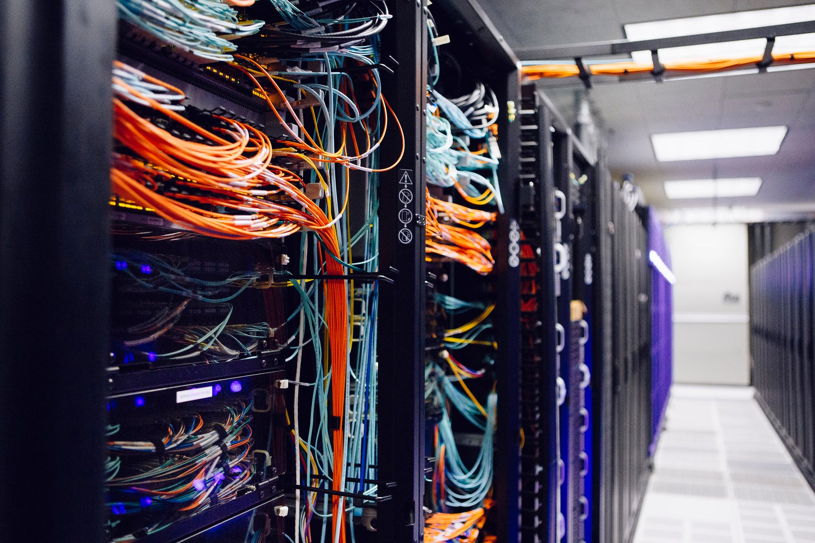 The inside of a supercomputer, showing a nest of brightly colored wires, mostly orange and black.