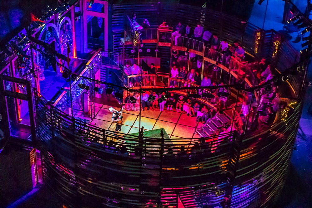 A colorfully lit amphitheater with someone playing guitar in the center