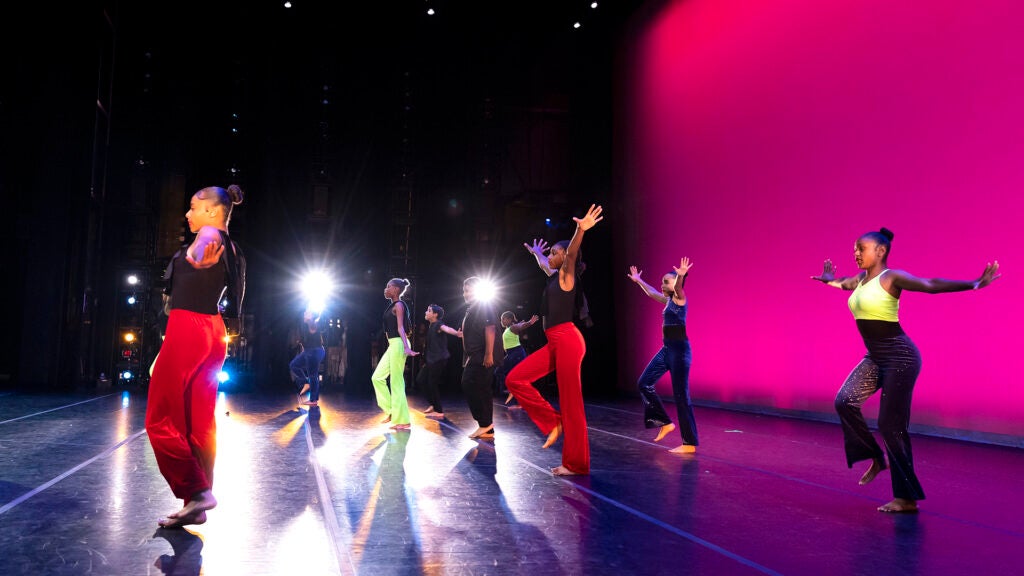Six student dancers perform on stage against a glowing pink curtain