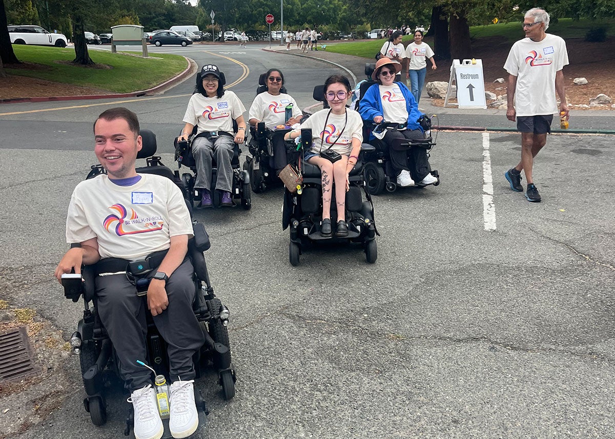 Ryan Manriquez and 7 other people at an advocacy event for Cure SMA, wearing matching t-shirts. Ryan and four fellow participants use motorized wheelchairs.