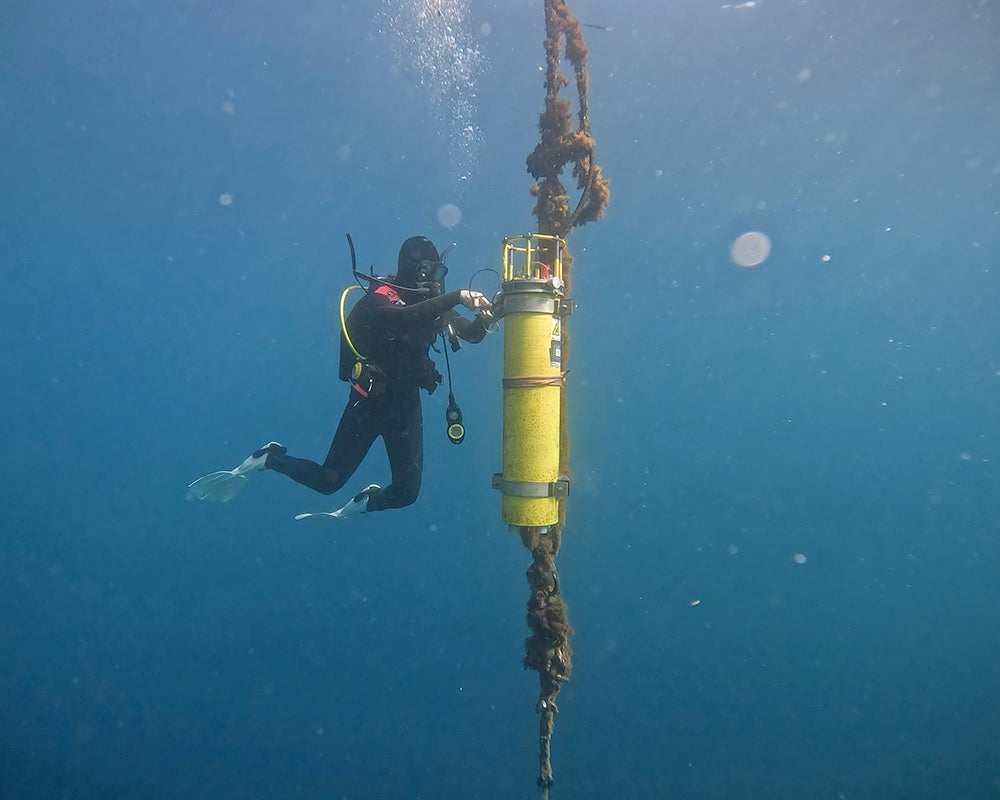 A SCUBA diver floats next to a yellow columnar instrument underwater