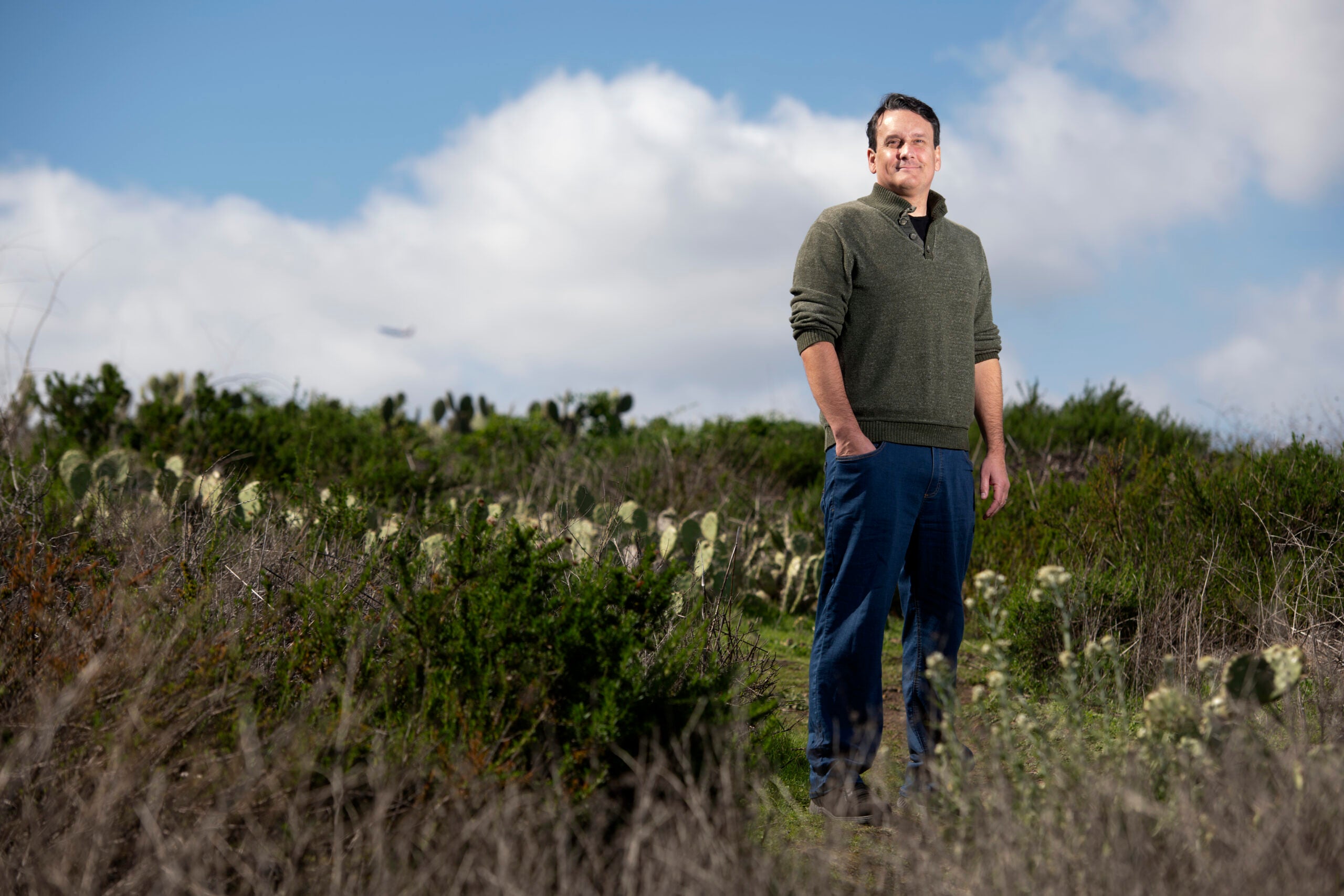 Bill Tomlinson, wearing jeans and a sweater, stands in a field