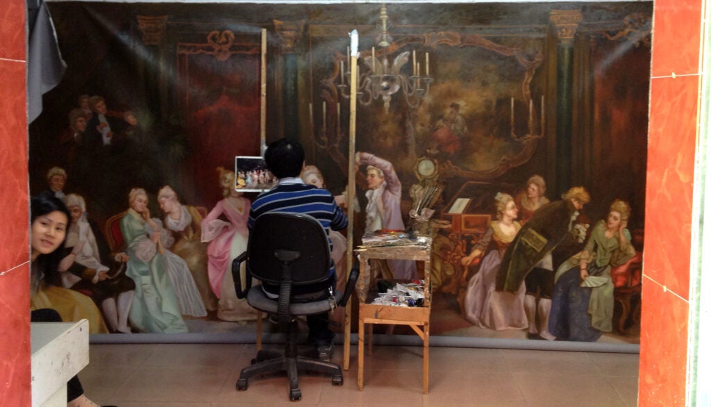 A man in a desk office chair paints a recreation of a famous, wall-sized artwork