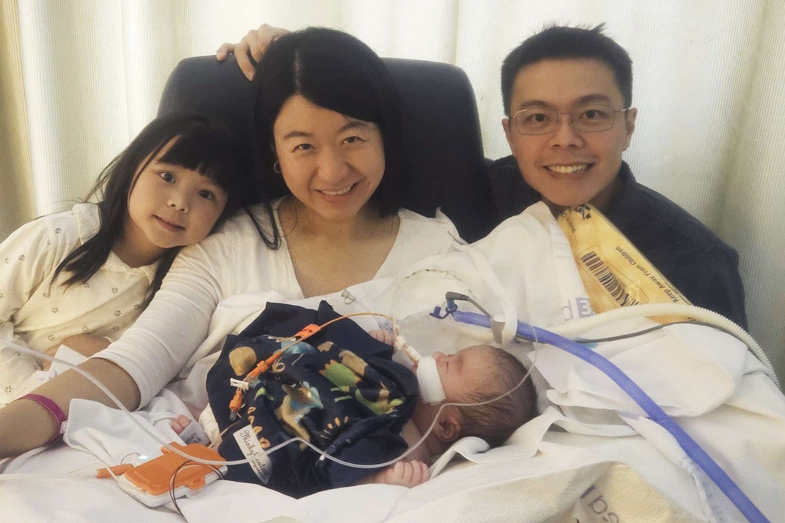 Mom, with a baby with a nasogastric tube on her lap, smiles for a photo with Dad and Big Sister.