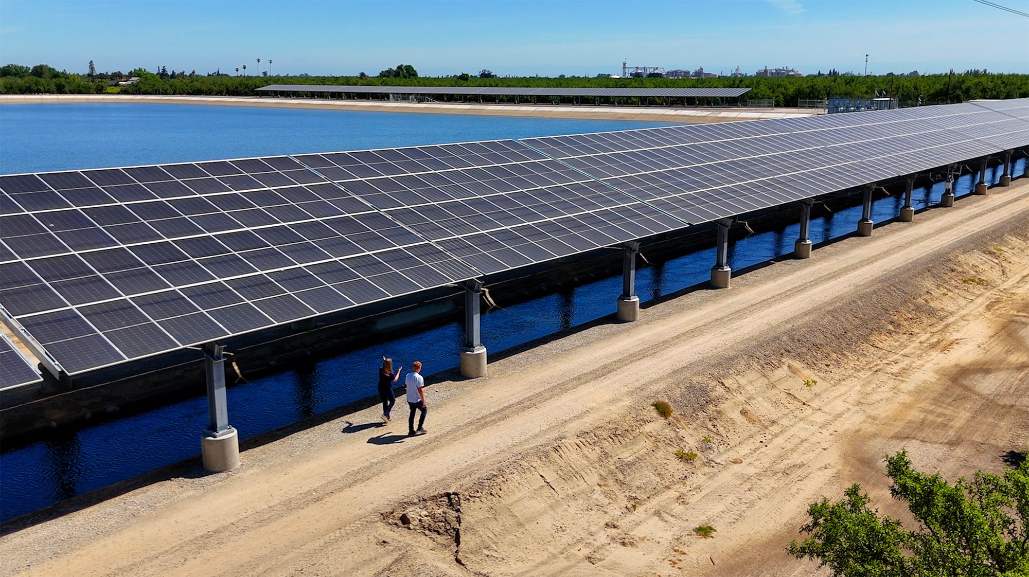 Two people walking along a series of solar panels over a canal in the Central Valley