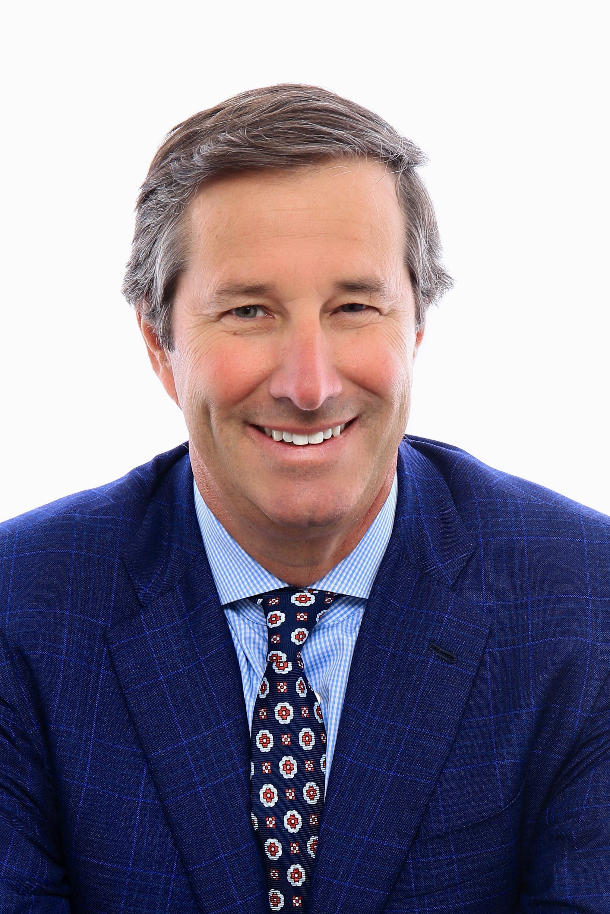 A man in a blue suit jacket and tie smiles