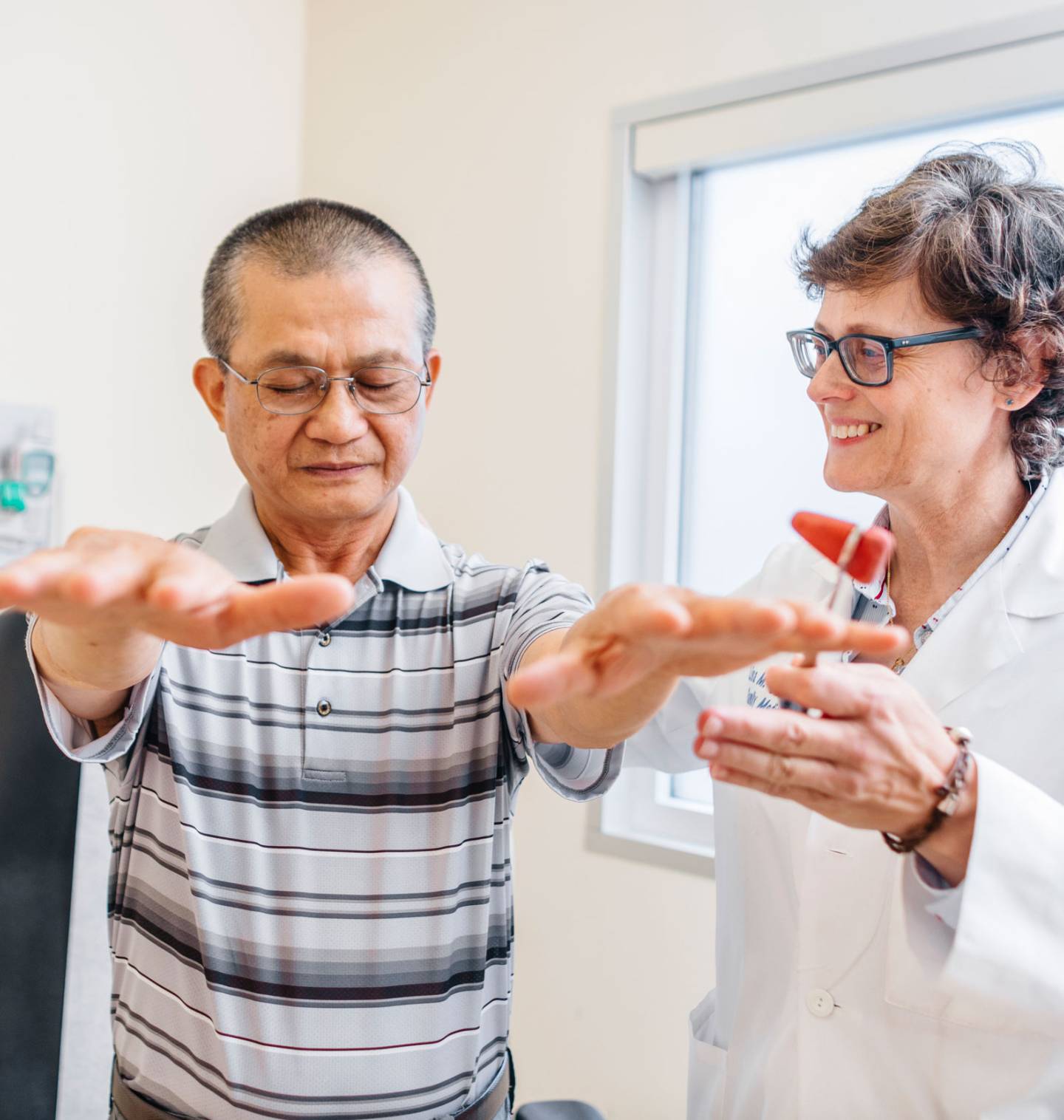 A man with outstretched arms is examined by a smiling healthcare professional.