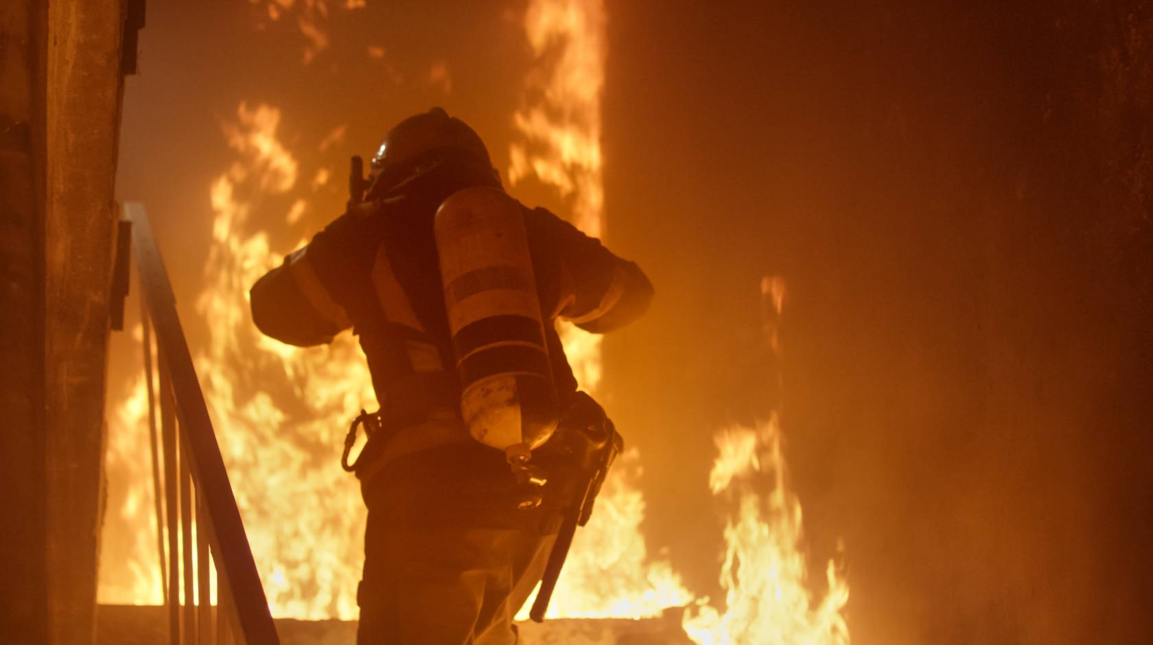 A firefighter with an oxygen cylinder runs up stairs on fire