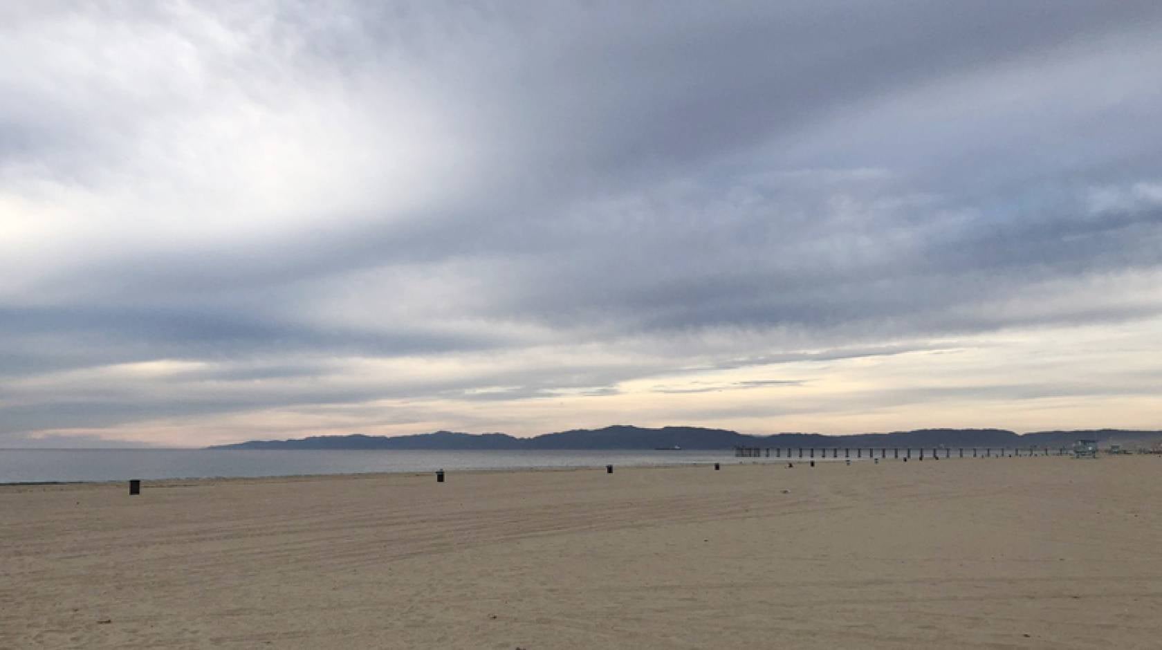 A wide-angle view of Hermosa Beach under a dramatic, cloudy sky