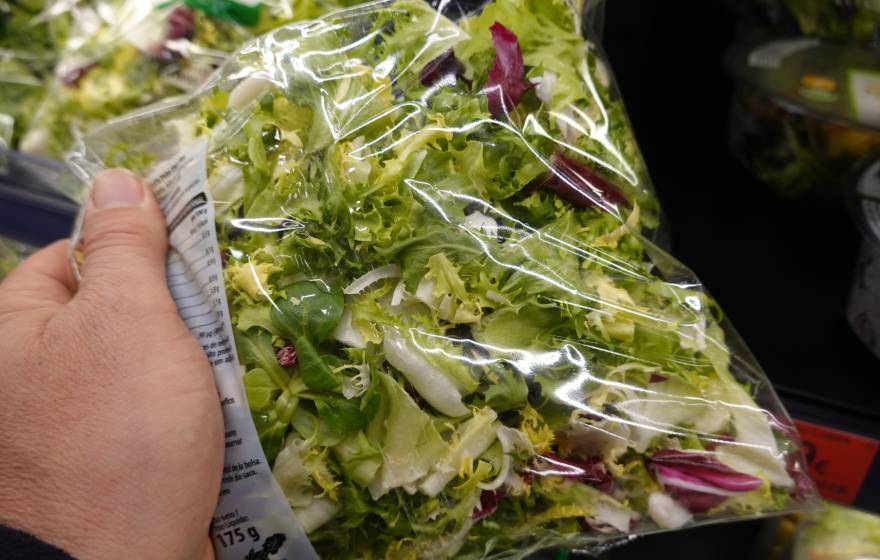 A hand holds a bag of salad greens at a grocery store