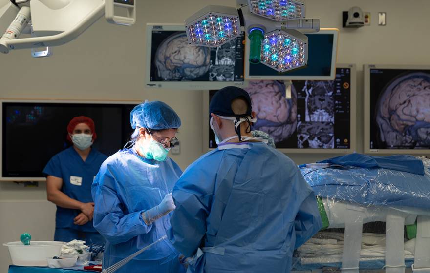 Surgeons operating in an operating room with brain scans hanging around the theater