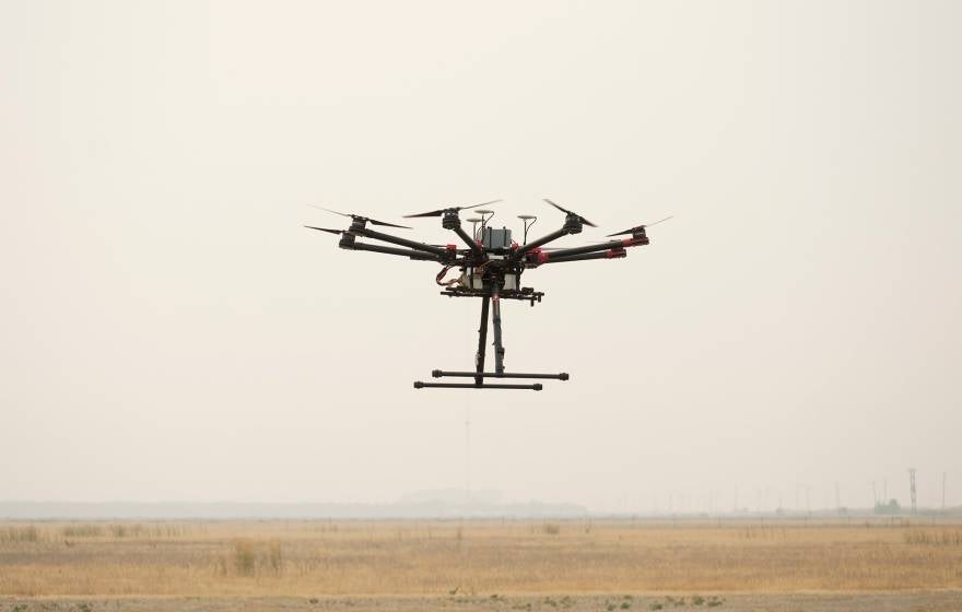 A drone hovers in smoky air over a field
