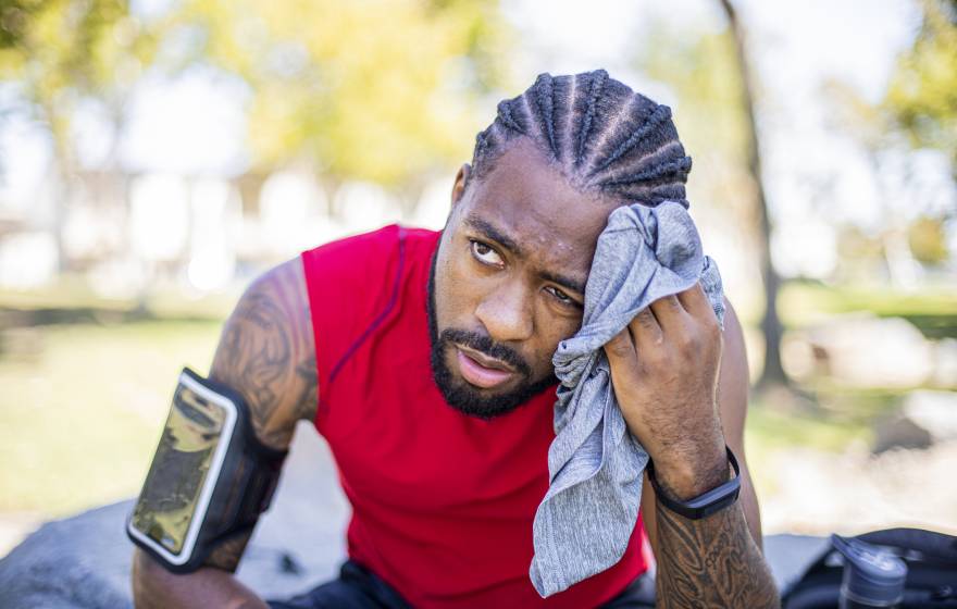 Young man wearing a phone on a sport band on his upper arm wipes sweat off his face and looks uncomfortable