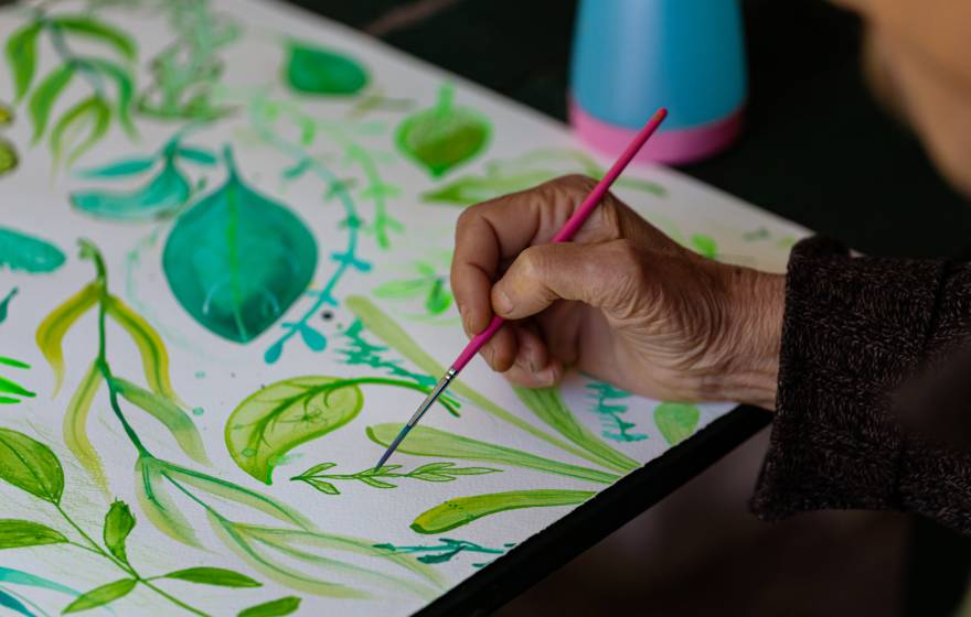 An older adult painting, hand on leaf decorative painting pictured